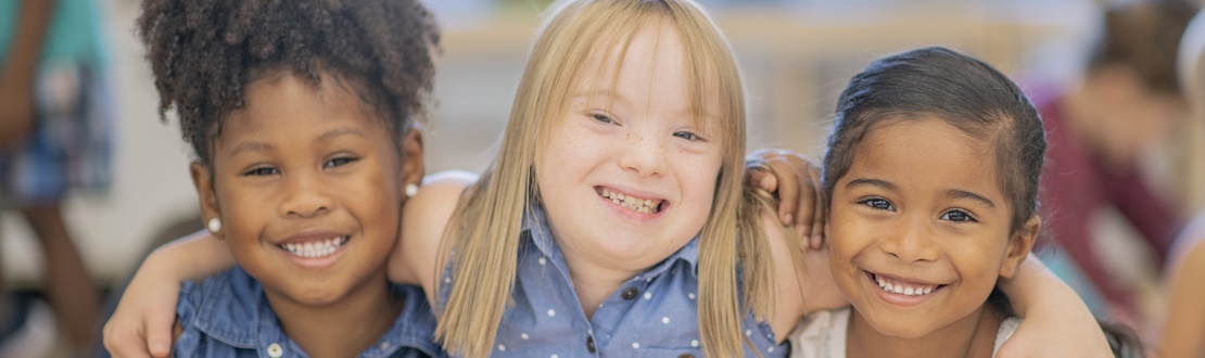 Three young girls sitting together, middle one has Downs Syndrome